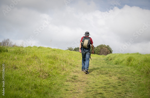 Man walking uphill under a stormy cloudy sky. Long Bay Coastal Walkway. Auckland.