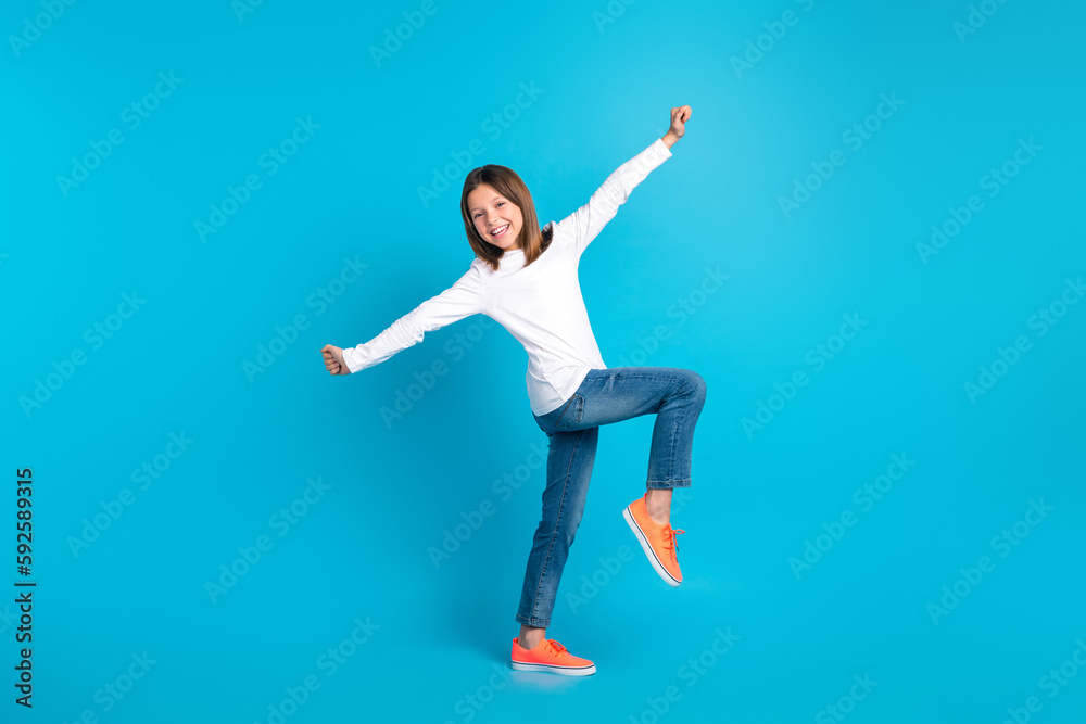 Full length photo of friendly funny schoolgirl dressed white shirt jeans sneakers dancing have fun isolated on blue color background