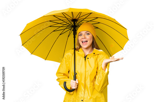 Young blonde woman with rainproof coat and umbrella over isolated chroma key background with shocked facial expression