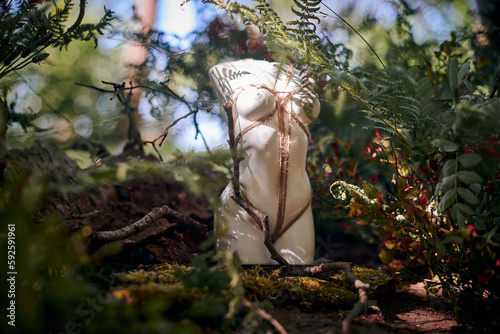 Female statue art object bound with rope in Japanese Shibari style in bushes outdoor green forest background, beauty of female body and nature concept. Limbless white woman figure tied with rope photo