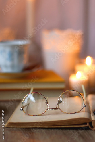 Cup of tea or coffee, plate of cookies, books, e-reader, pencil and lit candles on the table. Selective focus.