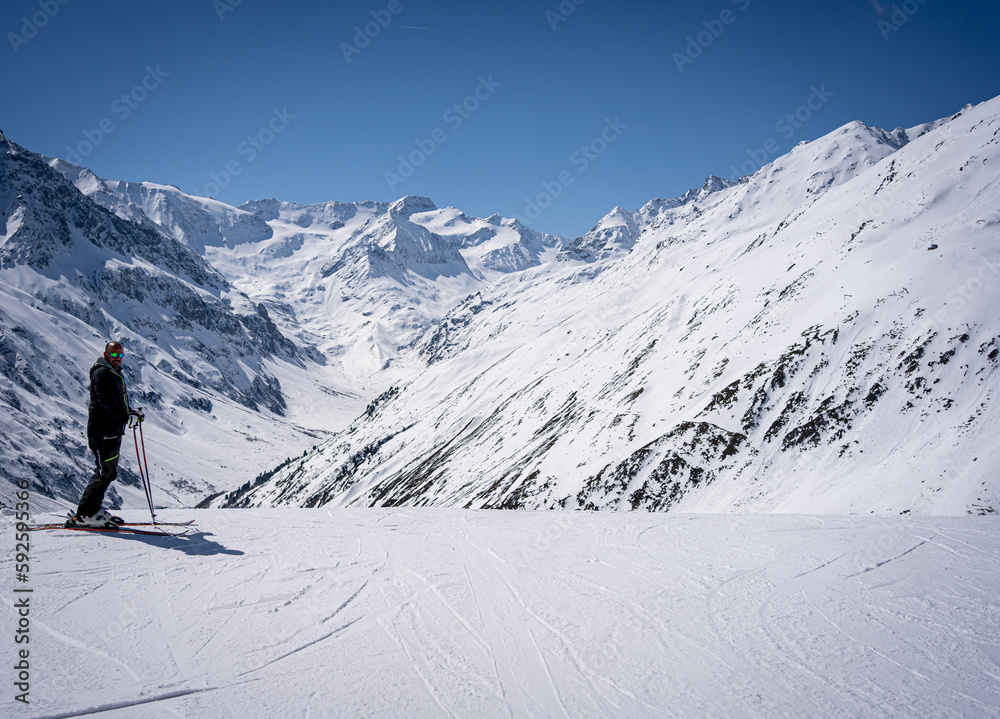 young man with ski makes pose in mountains behind