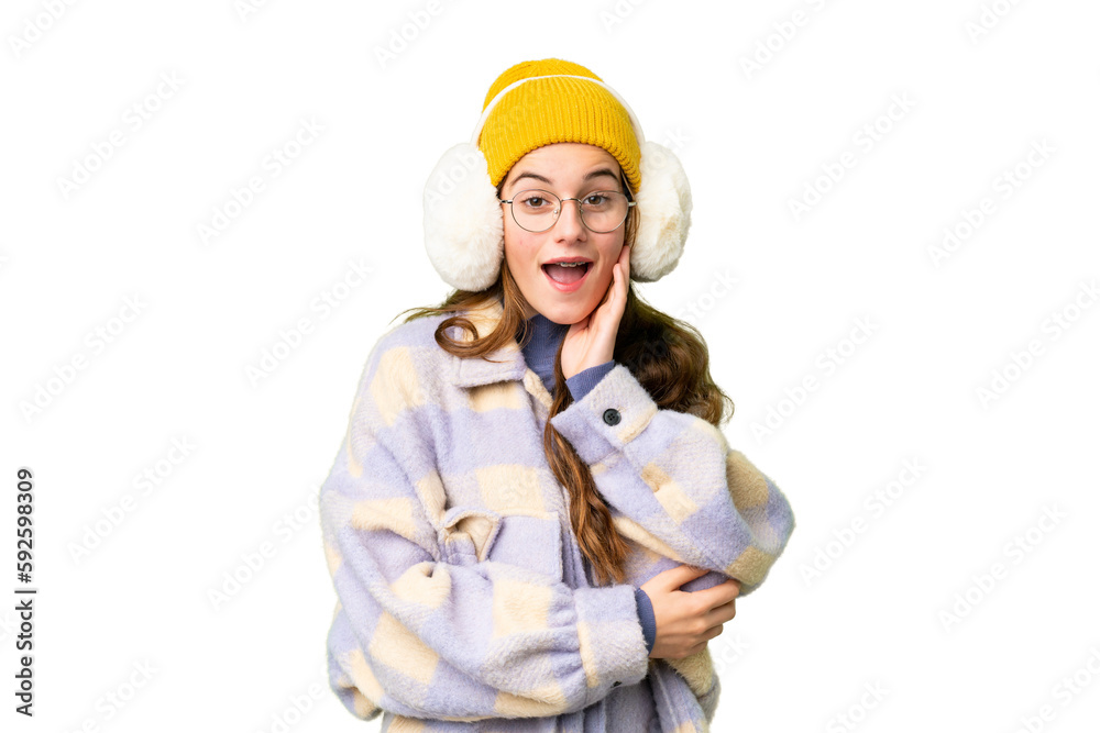 Teenager girl wearing winter muffs over isolated chroma key background surprised and shocked while looking right Teenager girl wearing winter muffs over isolated chroma key background surprised and shocked while looking right
