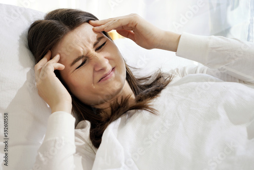 Woman in bed suffers from severe headache, migraine or depression and malaise