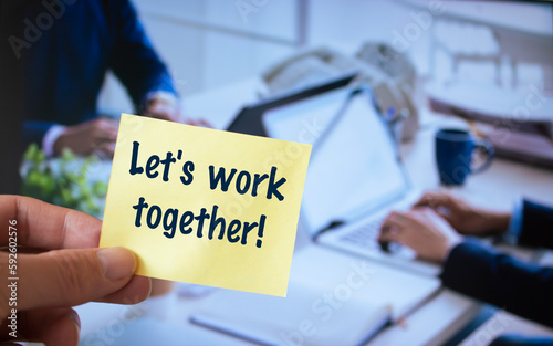 Male hand holding sticky note written Let's work together.