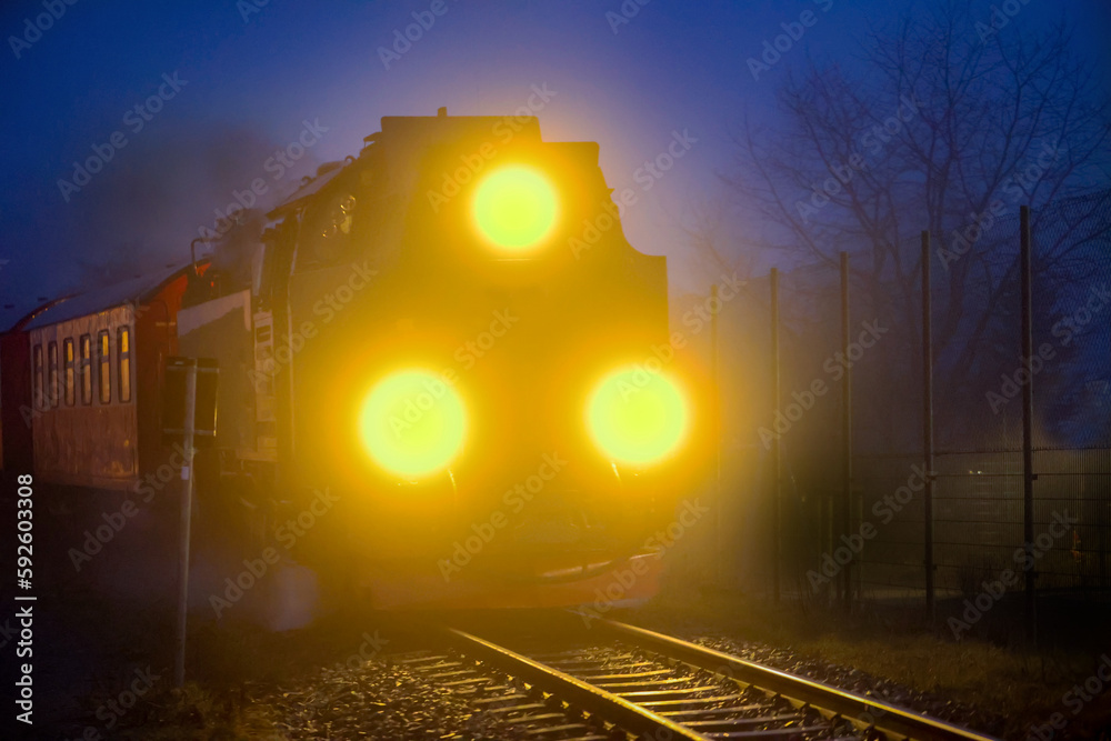 In einer neblig werdenen Nacht, fährt eine Dampflockomotive mit Zug.
