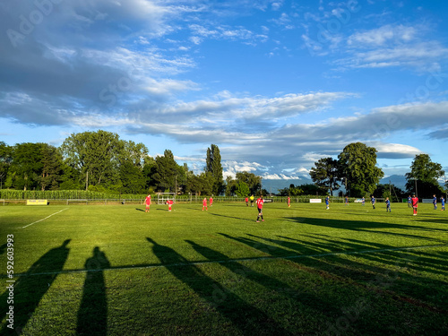 Football match with shadows of the spectators stretching across the pitch with blue sky and dramatic clouds