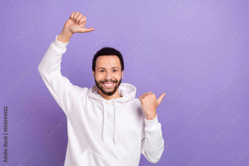 Photo of friendly man with curly hairstyle dressed white hoodie directing at offer empty space isolated on purple color background Photo of friendly man with curly hairstyle dressed white hoodie directing at offer empty space isolated on purple color background