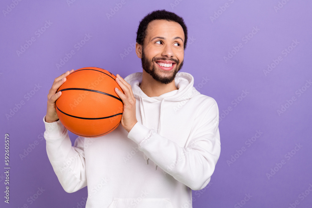 Portrait of positive minded man toothy smile hands hold basketball look empty space isolated on purple color background