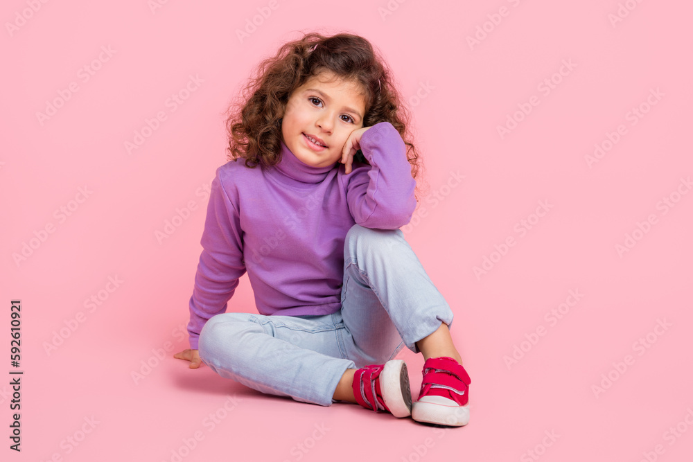 Full length photo of funky charming little child dressed purple pullover sitting floor smiling isolated pink color background Full length photo of funky charming little child dressed purple pullover sitting floor smiling isolated pink color background