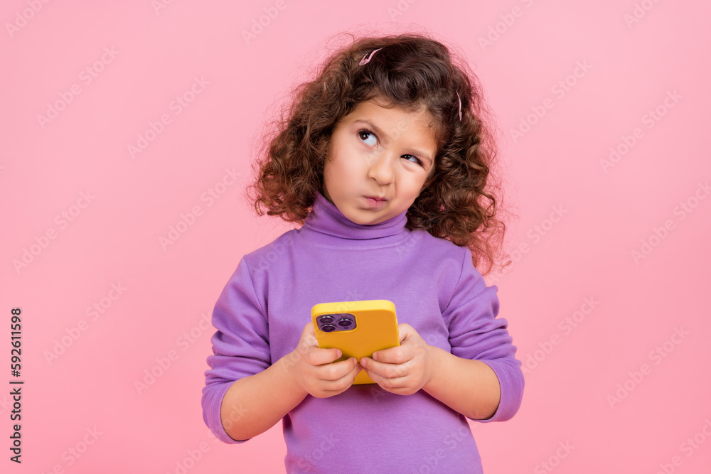 Photo of doubtful unsure little child dressed pullover typing apple samsung device looking empty space isolated pink color background Photo of doubtful unsure little child dressed pullover typing apple samsung device looking empty space isolated pink color background