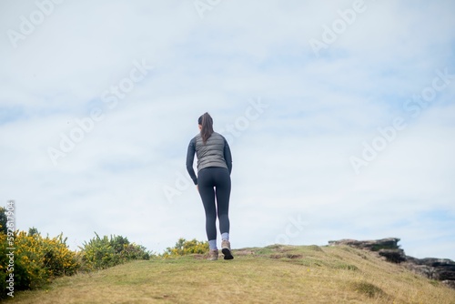 Back view of a female walking on a hill against cloudy sky