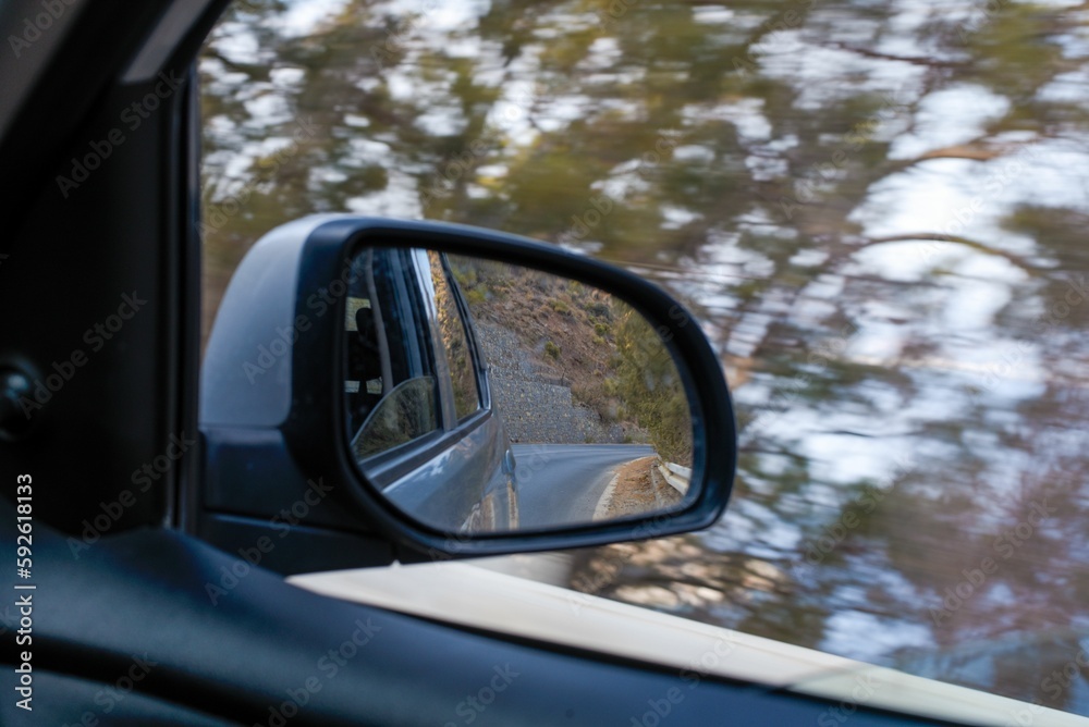 Closeup shot of car's sidemirror from inside the car while driving against blur nature background