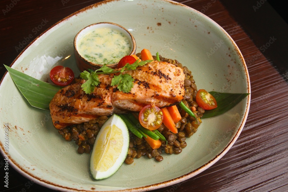 Closeup of delicious roasted salmon and lentil dish next to a sauce on a plate in a restaurant Closeup of delicious roasted salmon and lentil dish next to a sauce on a plate in a restaurant