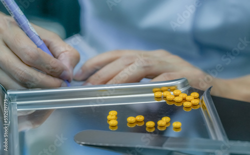 Yellow sugar coated tablet pill on stainless steel drug tray. Pharmacist hand holding pen and writing drug instructions on plastic pill pack. Prescription drug. World pharmacist day. Pharmacy concept. photo