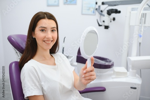 Woman looking in the mirror and smiling after checkup at dentist office.