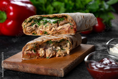 A delicious doner kebab wrap with meat, lettuce, tomato, onion and sauce on black background.