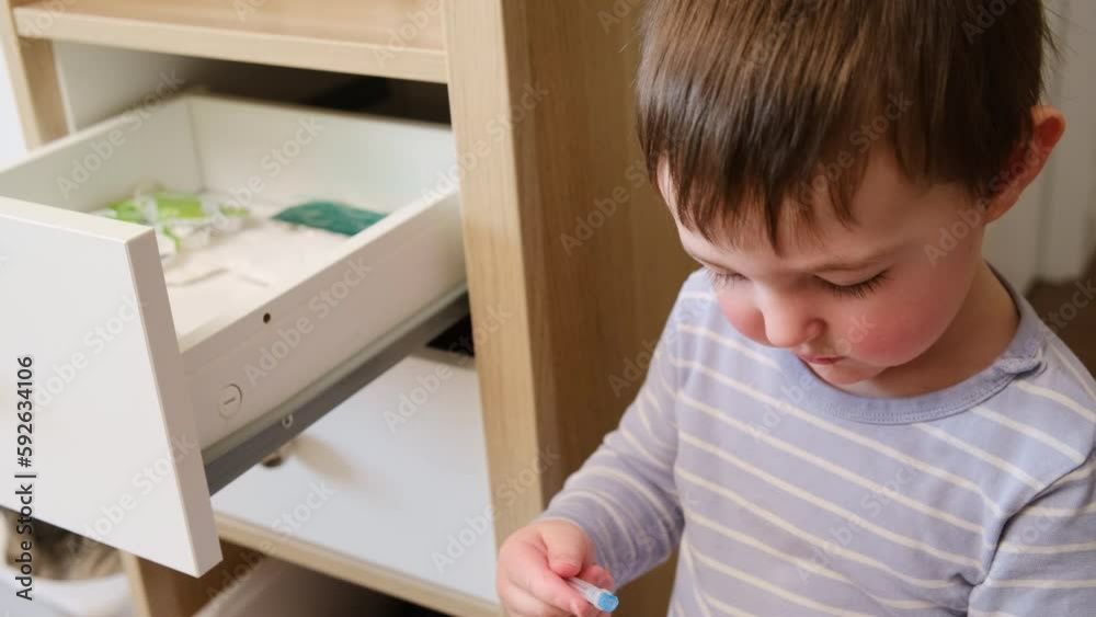 Toddler baby opened the cabinet drawer with syringe and medicine. Child boy holding a pack of pills in the home living room. Kid aged about two years (age one year nine months) Toddler baby opened the cabinet drawer with syringe and medicine. Child boy holding a pack of pills in the home living room. Kid aged about two years (age one year nine months)