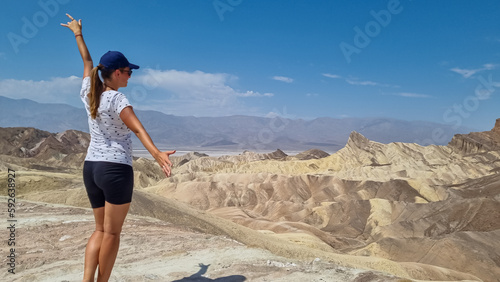 Woman with scenic view Badlands of Zabriskie Point, Furnace creek, Death Valley National Park, California, USA. Erosional landscape of multi hued Amargosa Chaos rock formations, Panamint Range in back