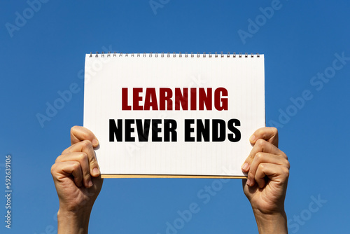 Learning never ends text on notebook paper held by 2 hands with isolated blue sky background. This message can be used as business concept about learning.