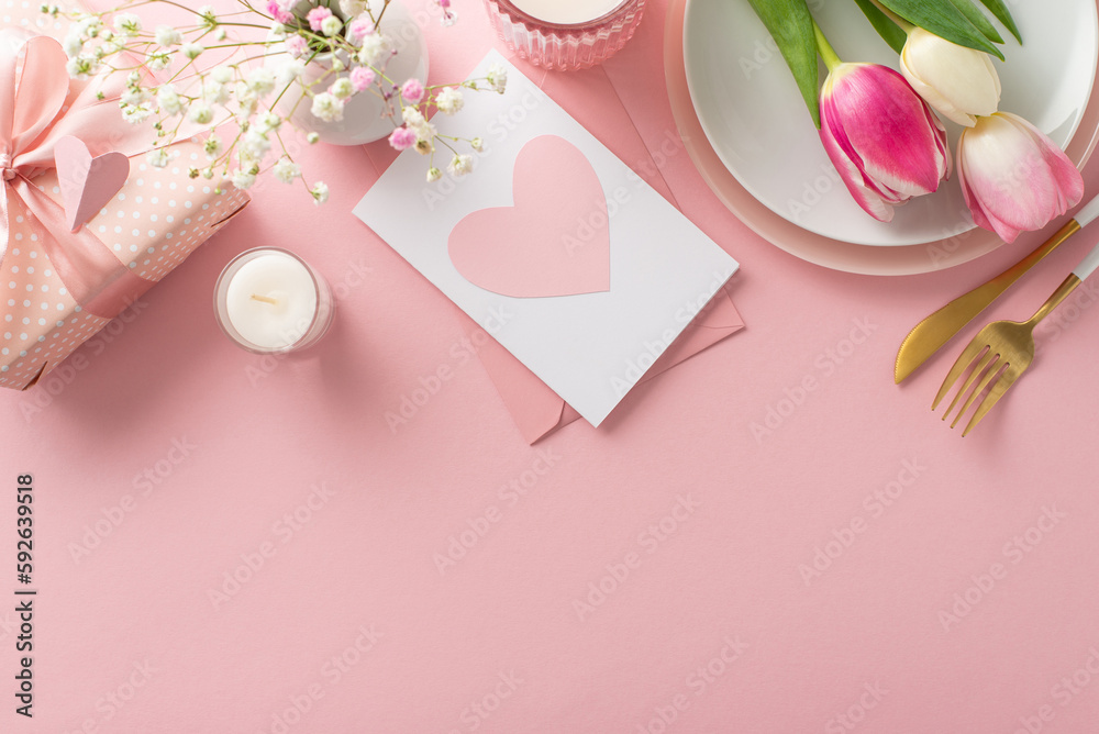 Minimalist Mother's day table arrangement. Top view flat lay of plates, cutlery, tulips, gift box, greeting card on pastel pink background with space for promotional text or advert