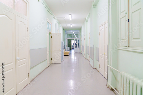 a hospital corridor with green walls and white doors and lamps on the ceiling.