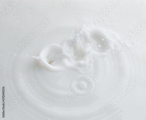 Cosmetic container white lotion droplet fly splashing. Milk lotion pour float to cosmetic bottle. Moisturizer lotion explosion spill. White background isolated high speed shutter freeze top view