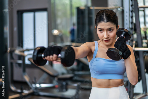 Confident young asian fitness woman doing exercises with dumbbells, Smiling girl doing sports indoors with dumbbells lifting weights. Fit fitness girl in sportswear exercising inside to slim down. © TeTe Song