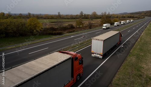 Convoys or caravans of transportation trucks passing on a highway on a bright blue day. Highway transportation with white and red lorry trucks.