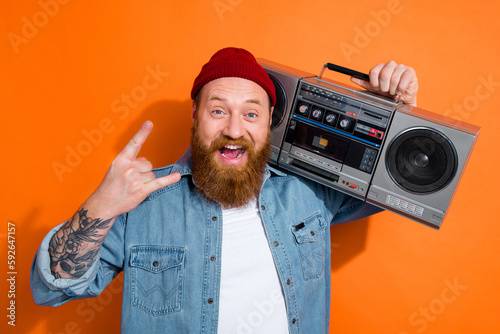 Photo of excited young brutal music lover man fingers punk symbol cassette player stereo stylish denim jacket isolated on orange color background