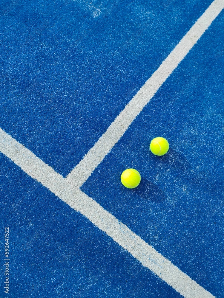 Vertical top view of two green balls on a blue artificial grass paddle tennis court by white line