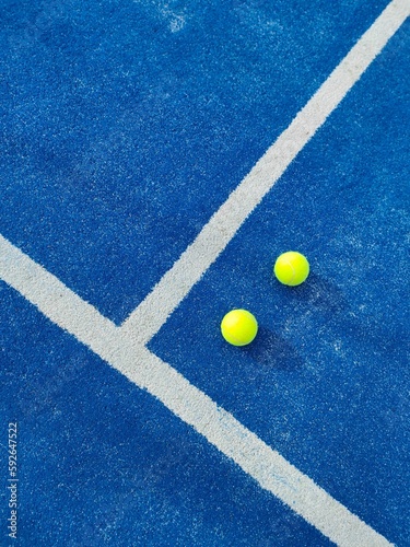 Vertical top view of two green balls on a blue artificial grass paddle tennis court by white line © Vicva/Wirestock Creators
