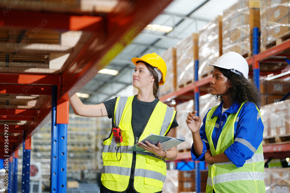 Multiethnic industrial workers checking their logistic lists while working with transportation of goods in warehouse Multiethnic industrial workers checking their logistic lists while working with transportation of goods in warehouse