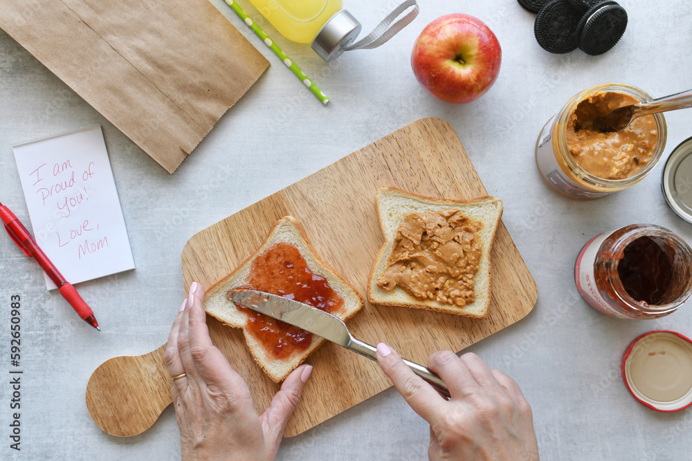 Mom making PB&J sandwich while packing lunch for child. Flat lay food ...