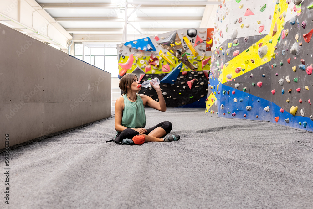 Young woman resting on cushion floor in gym and drinking water Young woman resting on cushion floor in gym and drinking water