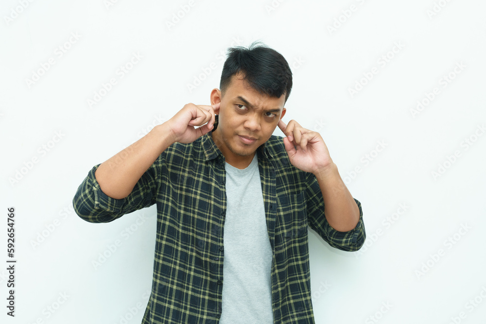 Young Asian man covering his ears using fingers avoiding noise Young Asian man covering his ears using fingers avoiding noise