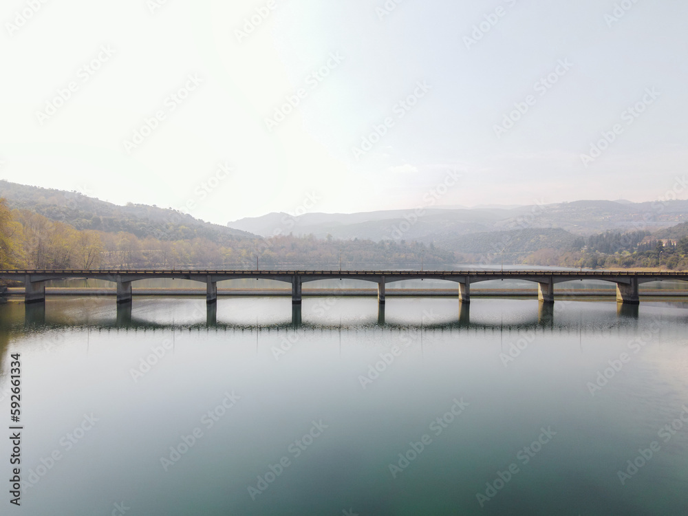 Drone photo of a bridge crossing a lake with beautiful caml water and mountains in the background at Veroia Greece
