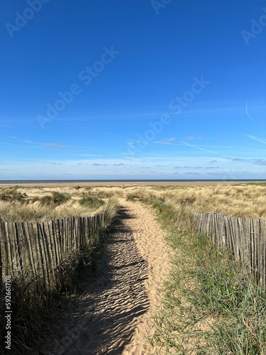 Fototapeta Naklejka Na Ścianę i Meble -  Pathway between the sand dunes leading onto the beach with a blue sky background. Taken in Lytham Lancashire England. 