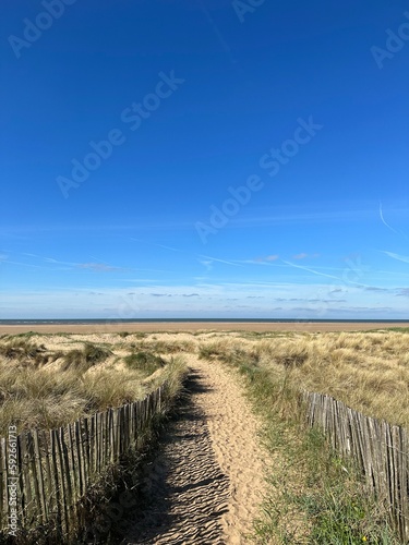 Pathway between the sand dunes leading onto the beach with a blue sky background. Taken in Lytham Lancashire England. 