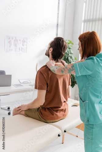 Εκτύπωση καμβά redhead osteopath touching painful back of man sitting on massage table in consulting room
