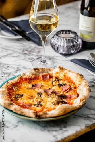 Vertical closeup of a pizza on the tablecloth with a glass of white wine near