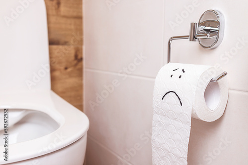 close-up sad emoticon on a roll of toilet paper hanging in the toilet room