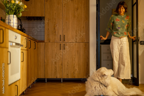 Woman walks in the kitchen room and greets her dog lying in stylish home interior. Domestic lifetyle concept photo