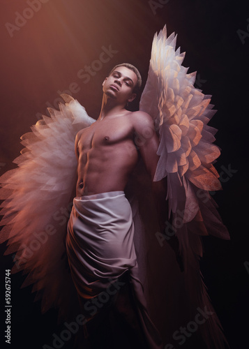 Young strong angel with white wings from heaven. Angel with muscular body. Sensual man