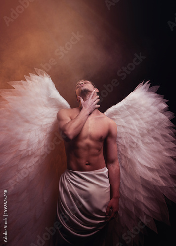 Young strong angel with white wings from heaven. Angel with muscular body. Sensual man