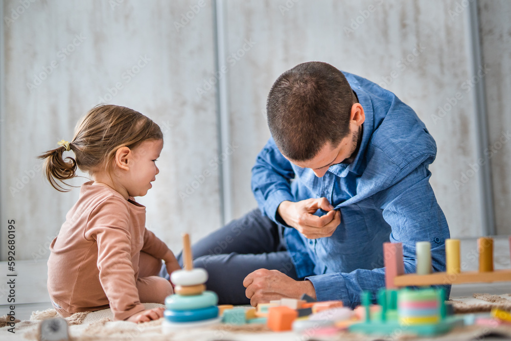 Naklejka premium One man caucasian playing at home with his daughter toddler on the floor with wooden toys, modern parenthood lifestyle single parent concept 