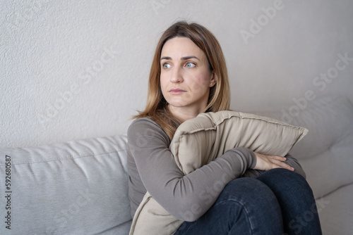 Portrait of lonely sad сaucasian young woman sitting on couch and hugs pillow.