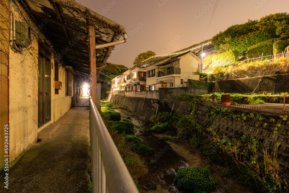 Walkway by dark river and old houses in small Japanese town at night