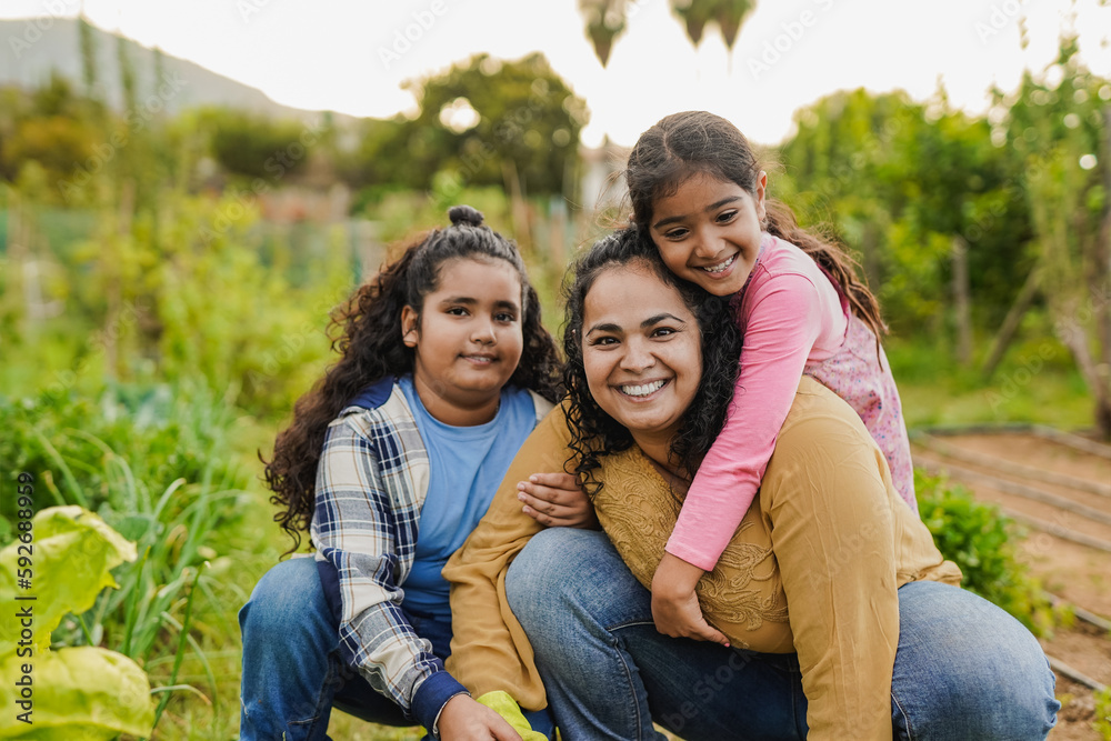 Fototapeta premium Happy indian mother having fun gardening with their children while smiling on camera - Harvest concept