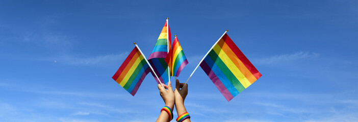 Rainbow flags showing in hands against clear bluesky, copy space, concept for calling all people to support and respcet the genger diversity, human rights and to celebrate LGBT in pride month.